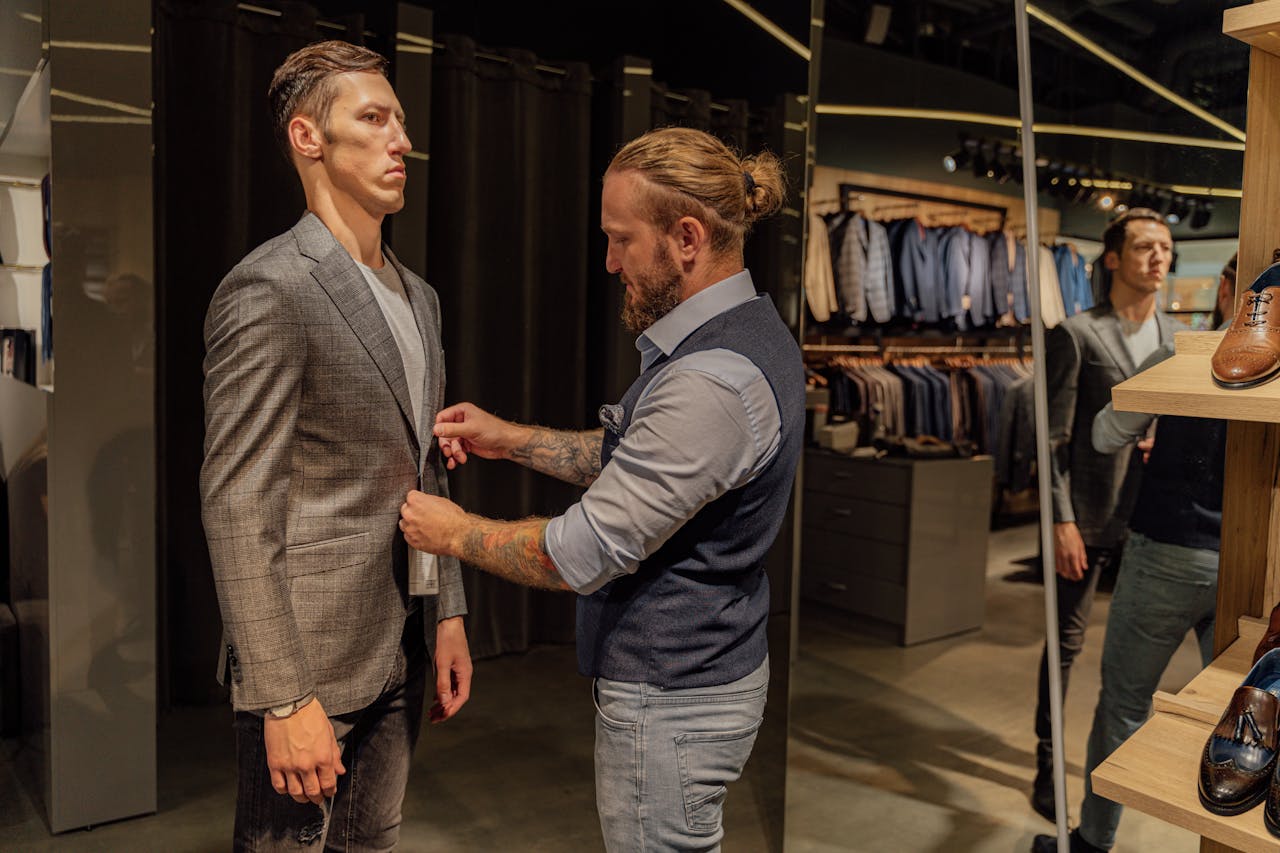why-choose-us A tailor adjusts a mans suit jacket in a modern fashion store.