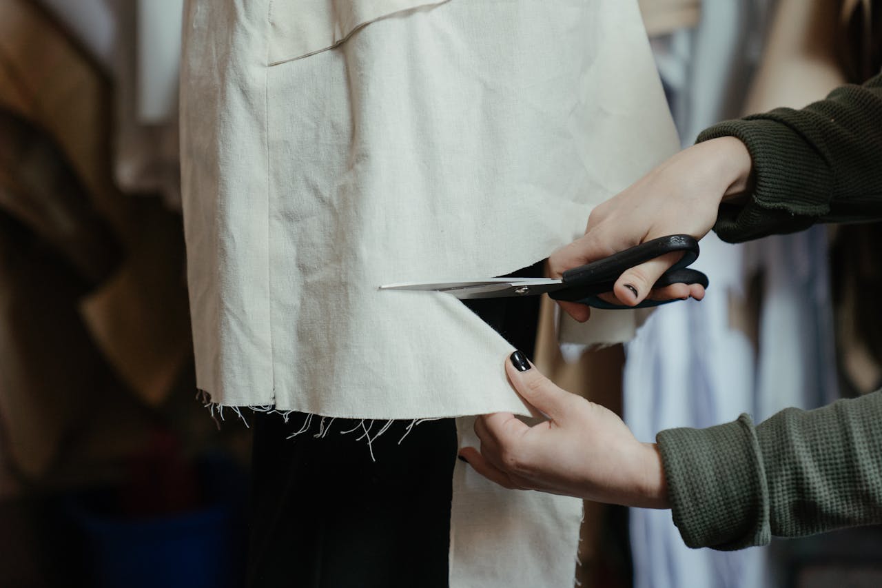 Hands cutting fabric with scissors in a workshop, showcasing the craft of tailoring and fashion design.
