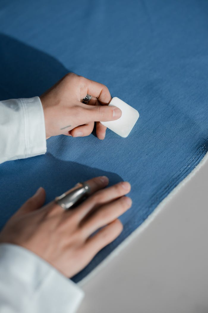 gallery-3 Close-up of a tailor marking blue fabric with chalk, showcasing craftsmanship.